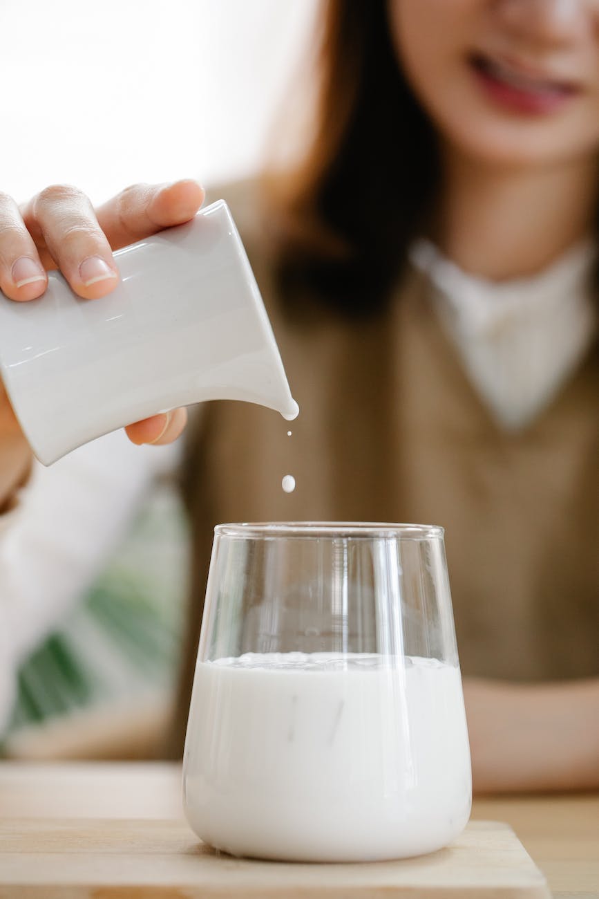 unrecognizable woman pouring milk from jug to glass
